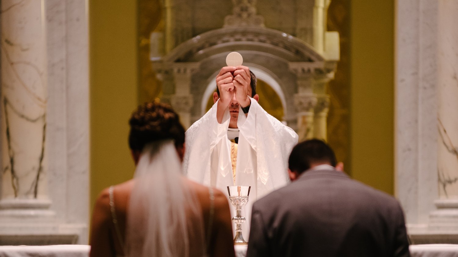 Zdjęcie przedstawiające parę młodą klęczącą przed księdzem.