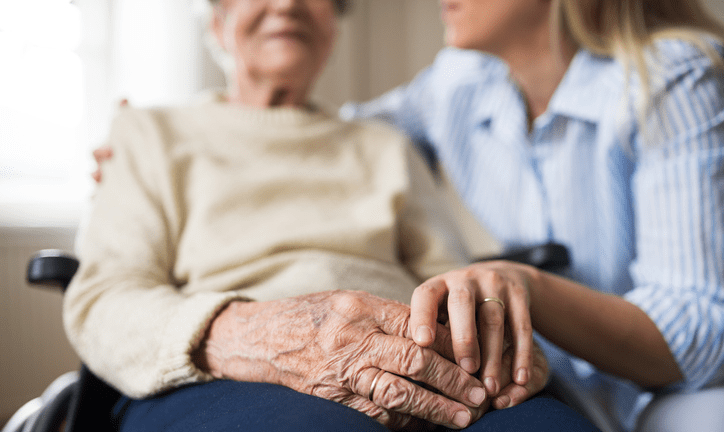 Elderly woman sitting in a wheelchair with a caregiver next to her.